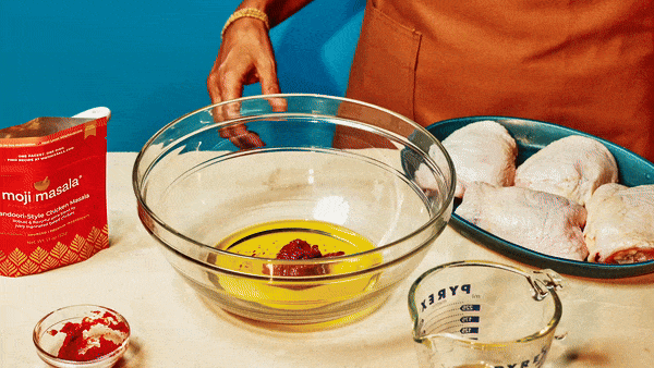 Hands mixing Indian spices into a marinade in a glass bowl — moji masala authentic Indian cooking